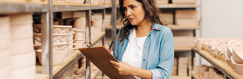 Female entrepreneur surrounded by inventory checking business milestones on clipboard.