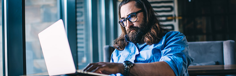 Male entrepreneur with shoulder length hair sitting in an office working on his computer. Exploring the business model canvas as a planning option.