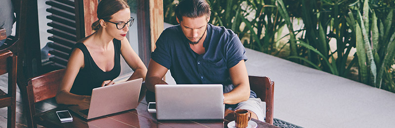 Male and female entrepreneurs sitting at a table outside of a coffee shop with laptops opening. Trying to figure out what to do before writing their business plan.